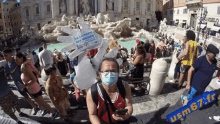 a man wearing a mask stands in front of a fountain with a sign that says " la langue des signes "