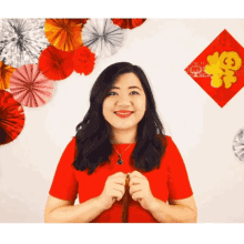 a woman in a red shirt stands in front of a wall with paper fans and a chinese symbol on it