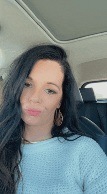 a woman in a white sweater and earrings is sitting in a car