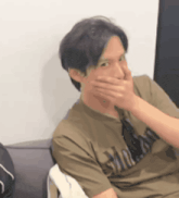 a man is covering his mouth with his hand while wearing a t-shirt that says ' army ' on it