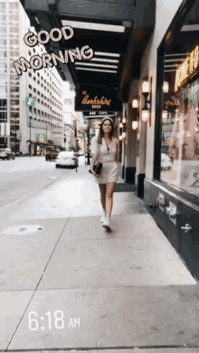 a woman is walking down a sidewalk in front of a building with a sign that says " good morning "