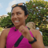 a woman wearing a pink tank top and sunglasses smiles