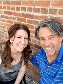 a man and a woman are smiling in front of a red brick wall