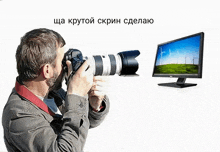 a man is taking a picture with a camera and a computer monitor is behind him