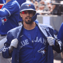 a man wearing a blue jays jacket and helmet takes off his jacket