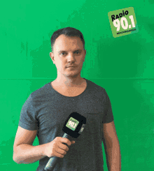 a man holds a microphone in front of a green background that says radio 90.1