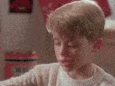 a young boy in a white sweater is crying while looking at a book .