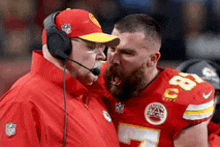 a man wearing a headset is talking to a football player on a field .