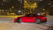 a red car is driving in the snow at night