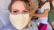 a woman is wearing a crocheted face mask while sitting on a plane with two children .