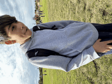 a young boy wearing a grey sweatshirt and a black adidas backpack stands in a grassy field