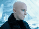 a bald man with blue eyes wearing a black fur coat