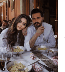 a man and woman are sitting at a table with plates of noodles