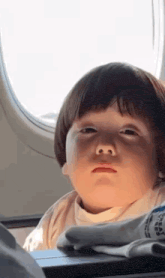a little girl is sitting in an airplane looking out the window .