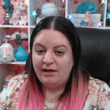 a woman with pink hair is sitting in a chair in front of a shelf with stuffed animals on it .