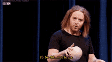 a man with long hair and a beard is holding a ball and says to be or not to be