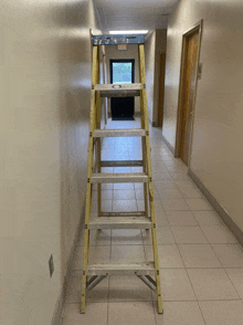 a ladder in a hallway with a red exit sign on the wall