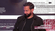 a man with a beard is standing in front of a screen that says l' indic de la redac