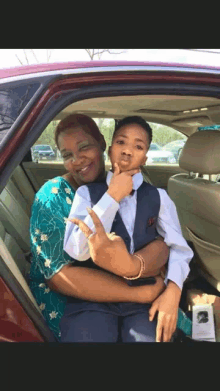 a woman is holding a young boy in her lap in the back of a car .