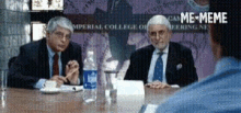 two men are sitting at a table with water bottles in front of a sign that says imperial college of meringney