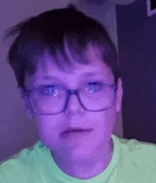 a young boy wearing glasses and a green shirt is making a face .