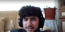 a man wearing headphones is sitting on a couch with a potted plant in the background