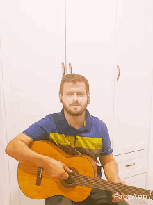 a man with a beard is holding a guitar in front of a white cabinet