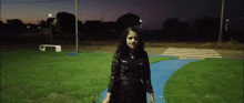 a woman in a black dress is standing on a grassy path at night