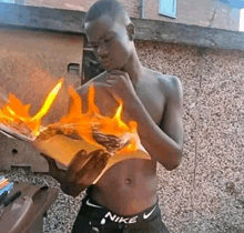 a shirtless man in nike underwear is holding a piece of paper that is on fire .