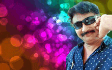 a man wearing sunglasses and a blue shirt is standing in front of a rainbow background .