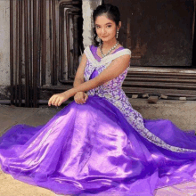 a young girl in a purple dress is sitting on the ground