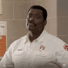 a man in a white uniform with a badge that says chicago fire is standing in front of a brick wall .