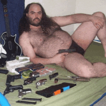 a shirtless man is laying on a bed with a gun in his hand