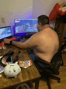 a man sits at a desk playing a video game while a piggy bank sits on the desk