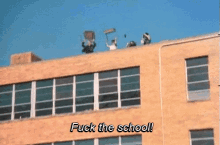 a group of people on the roof of a building with the words " fuck the school " written below them