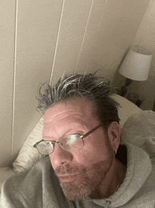 a man wearing glasses and a gray sweatshirt is laying on a bed