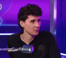 a man in a black shirt stands in front of a microphone with a purple background