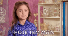 a little girl in a blue shirt is standing in front of a shelf with a shelf full of trophies .