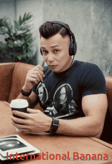 a man wearing headphones sits at a table holding a cup of coffee and looking at his phone