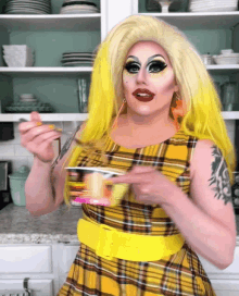 a drag queen in a plaid dress is holding a cup of food