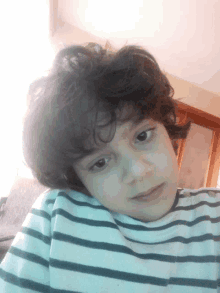 a young boy with curly hair wearing a striped shirt looks at the camera