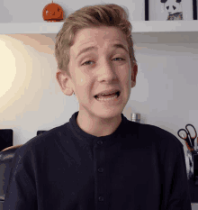 a young boy making a funny face in front of a shelf with a pumpkin on it