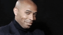 a man in a suit and turtleneck is smiling .
