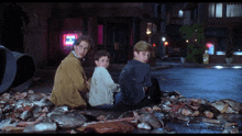 a man and two children sit on a pile of fish in a city street