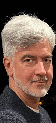 a man with gray hair and a beard looks at the camera