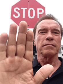 arnold schwarzenegger shows his hand in front of a stop sign