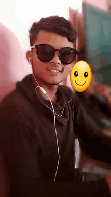 a young man wearing sunglasses and ear buds has a smiley face behind him