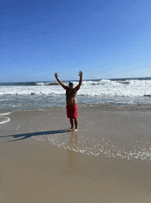 a man in red shorts is standing on a beach with his arms outstretched