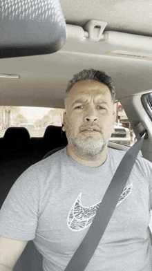 a man with a beard wearing a grey nike shirt is sitting in a car