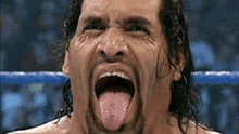 a wrestler is sticking his tongue out while standing in a wrestling ring .